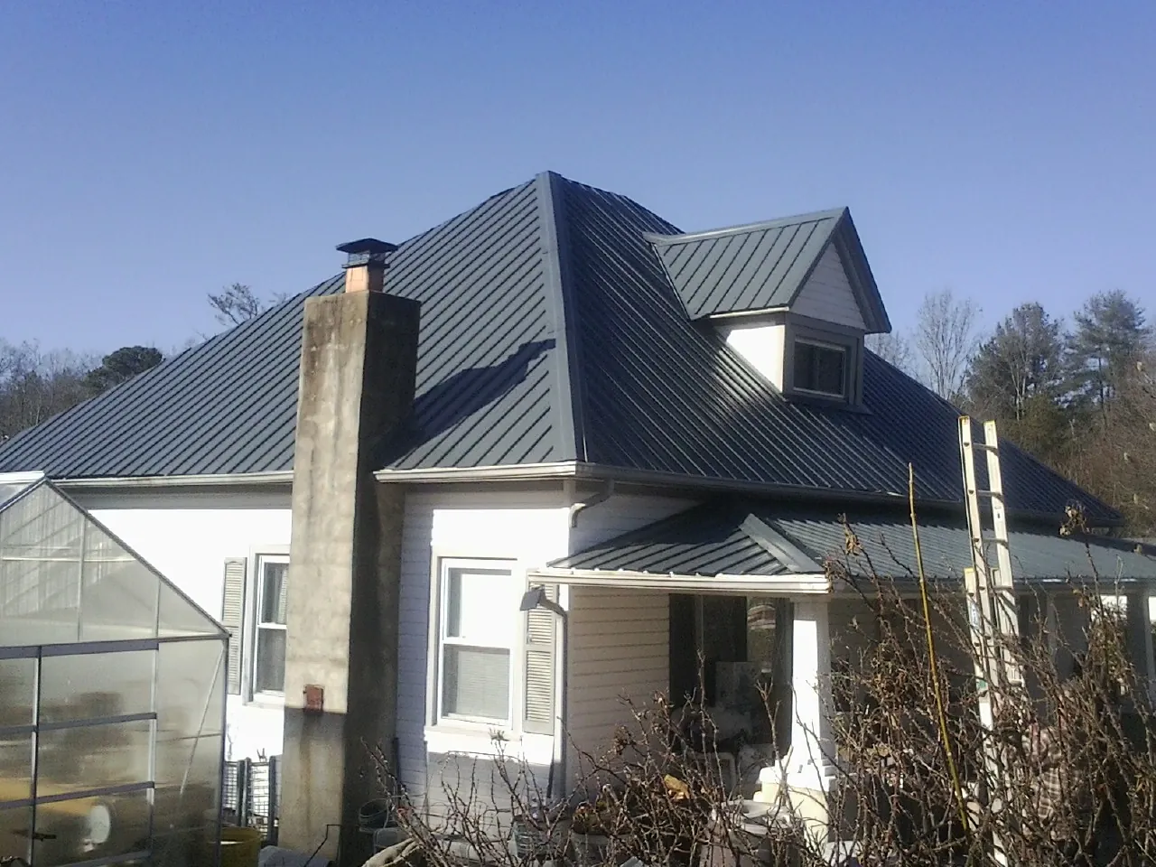 Dark blue standing seam metal roof on a white farmhouse with dormer — Slate & Tile Roof Repair by Roofing Brothers in Nortonville