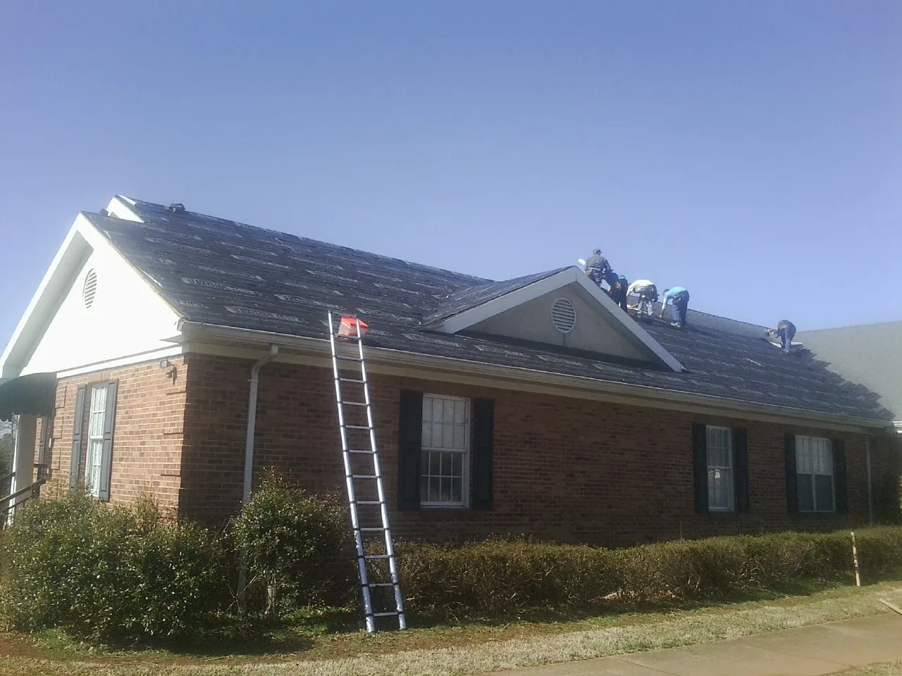 Crew tearing shingles off a brick ranch roof with a ladder set — Metal Roof Repair work by our crew in Nortonville