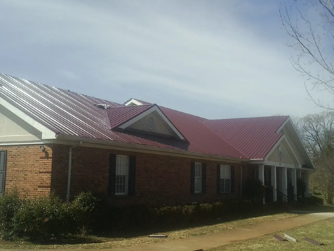 Red metal roof with gabled entries on a long brick building, from a Hail Damage Roof Repair job in Nortonville