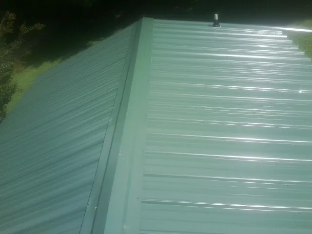 New green metal panels meeting at the ridge of a roof — Flat Roof Repair work by our crew in Nortonville